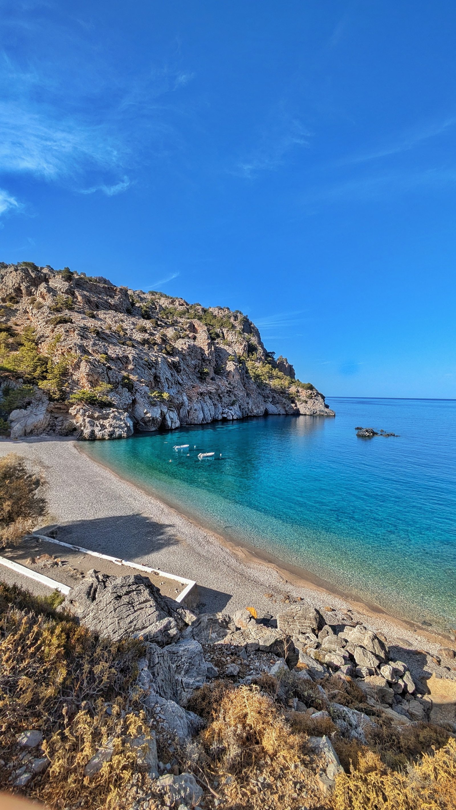 Piccola spiaggia deserta con acque calme e montagne sullo sfondo in una cala di Karpathos