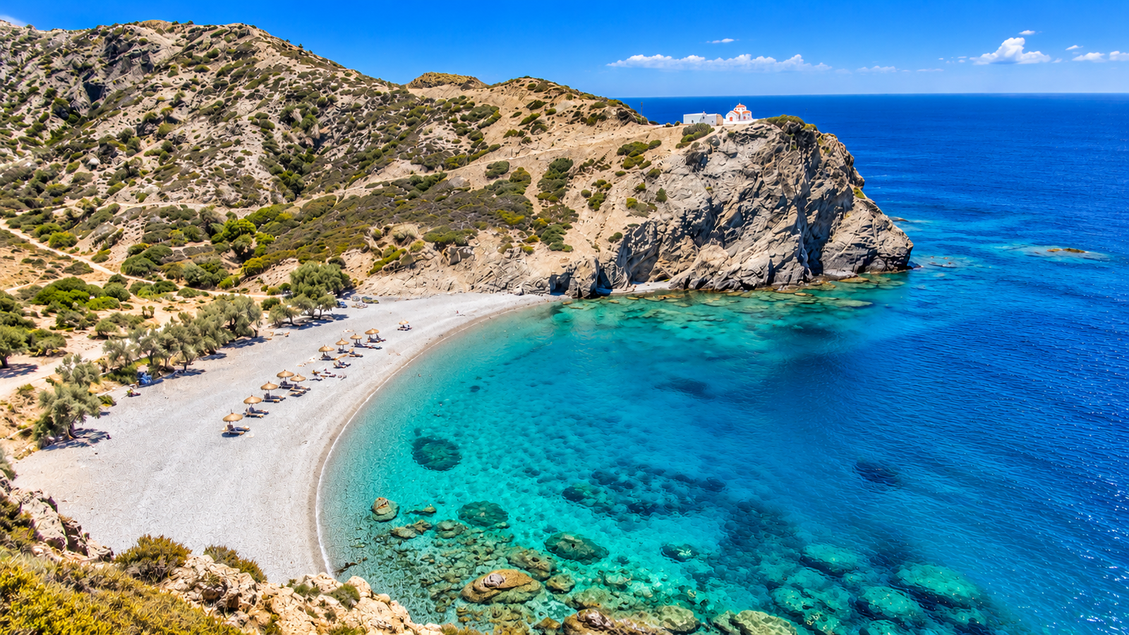 Spiaggia isolata di ciottoli con acqua blu profondo circondata da rocce